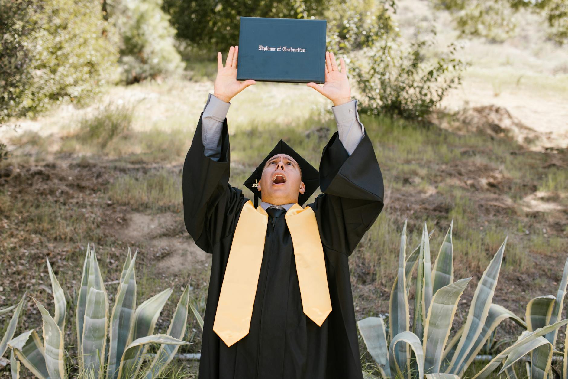 student in a graduation gown holding up his diploma